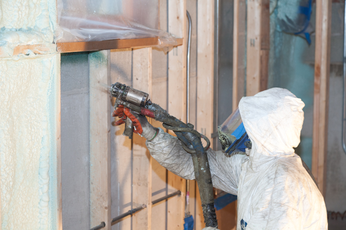 Spraying spray foam insulation into the framing of a home to improve the home's air sealing qualities.