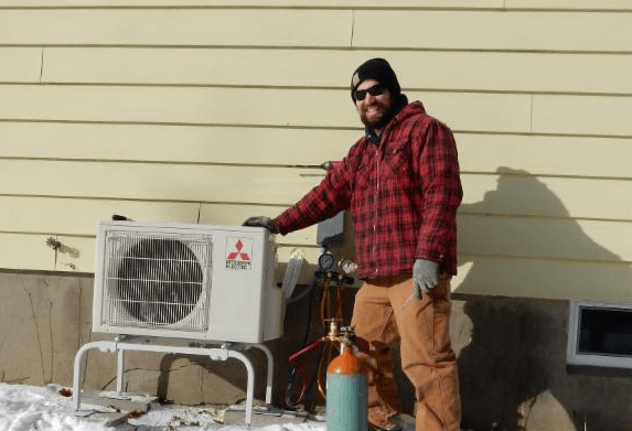 Man standing next to a heat pump in the cold weather of Vermont.