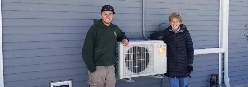 Two people standing next to a cold weather heat pump
