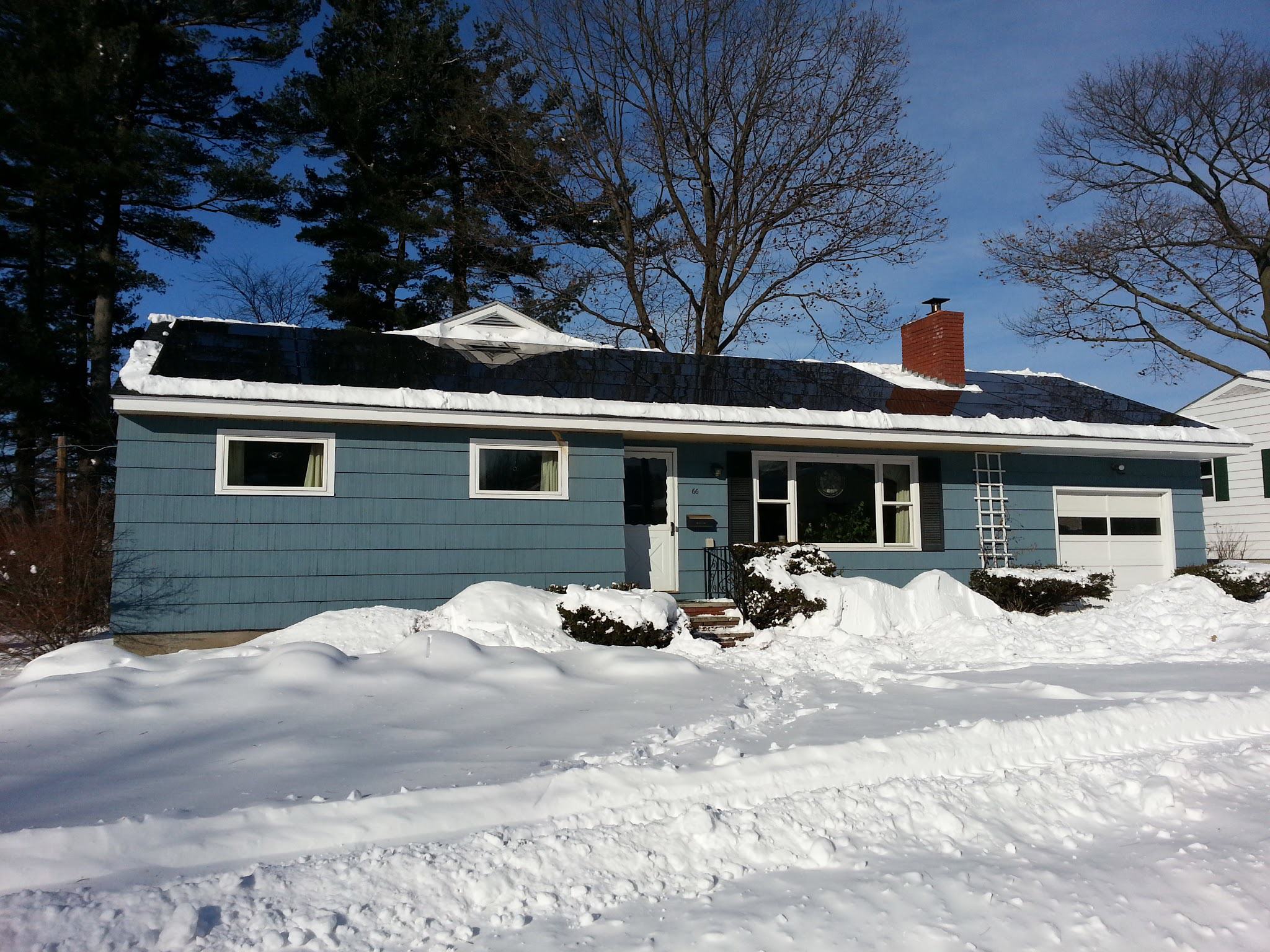 A small ranch home in Vermont with snow on the yard and roof, however the solar panels are free of snow.
