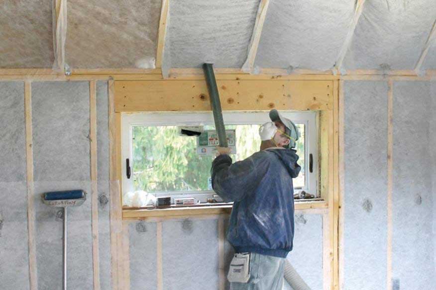 A worker utilizing a hose to install dense pack cellulose insulation into the framing of a home to help with the insulation and energy efficiency of this new home.