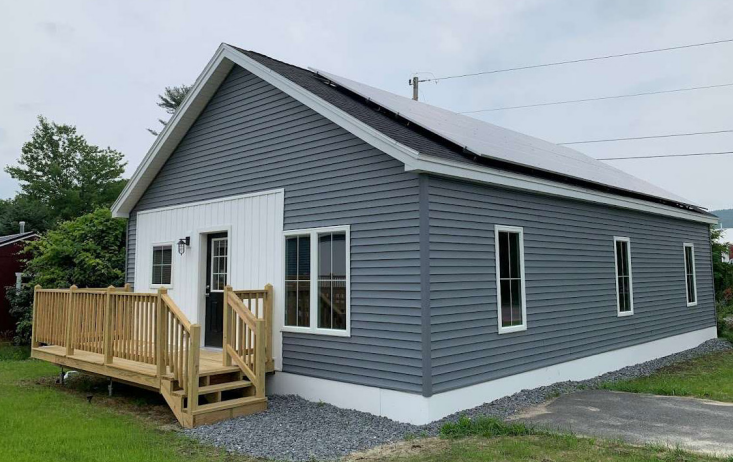 Large photovoltaic solar panels line the roof of a small house, providing energy for this unit and bringing energy efficiency to a property in Bradford, VT.